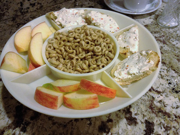 White bowl plate with apple slices and bread with spread on the plate sections and ring cereals on the bowl
