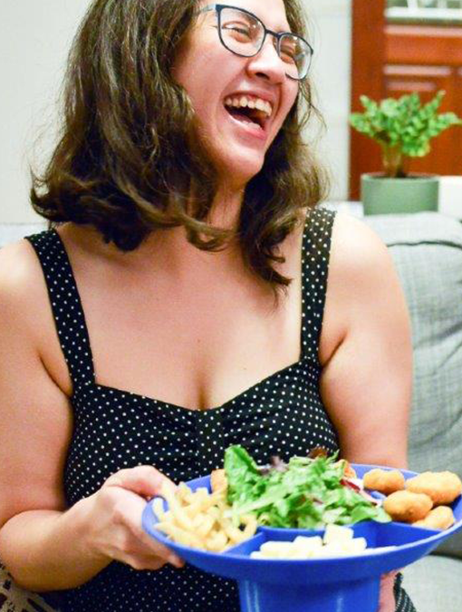 Bespectacled woman in a polka-dotted dress holding a bowl plate filled with chips