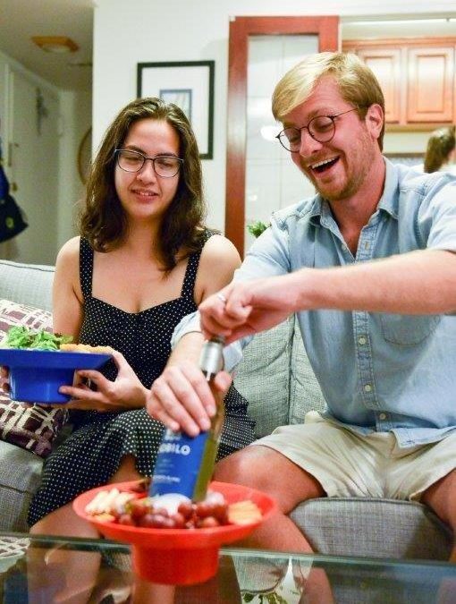 Bespectacled man opening a liquor bottle from a bowl plate filled with ice while sitting next to a wavy-haired woman